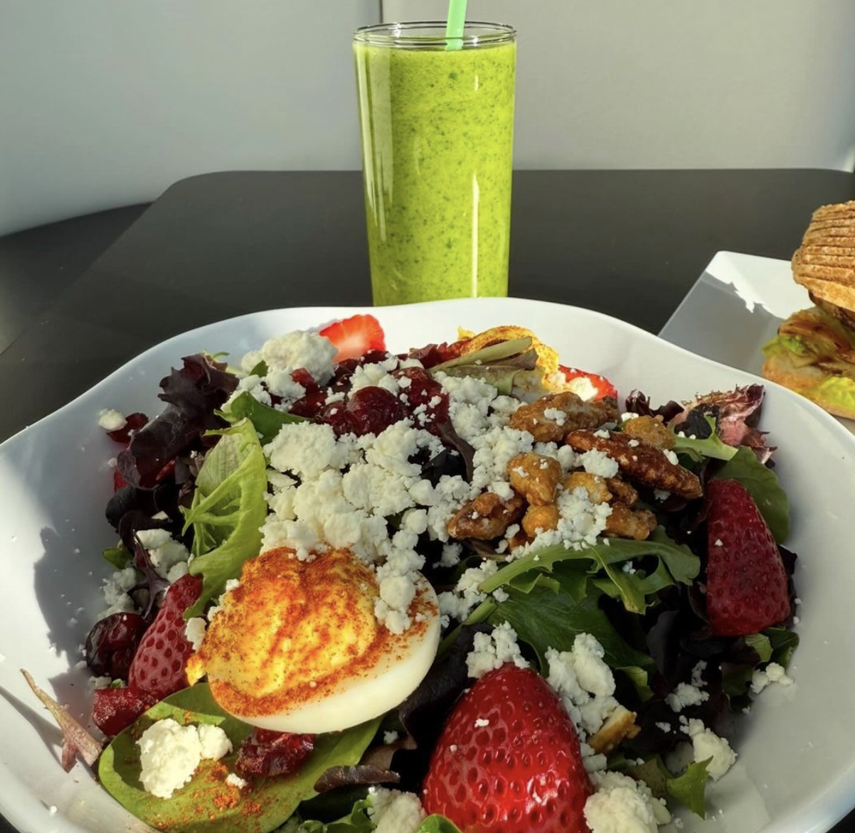 A salad with strawberry, an egg and light cheese. Behind it is a green smoothie with a green straw